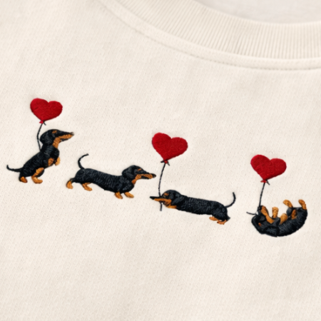 Embroidered design of four dachshunds holding heart-shaped balloons on a white fabric.